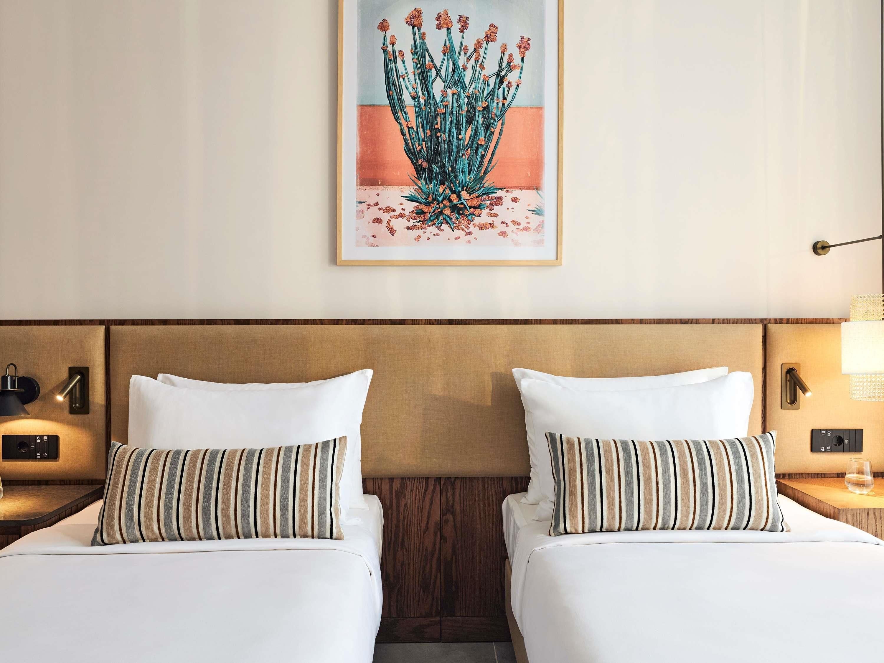 Een hotelkamer met twee bedden, een nachtkastje met een lamp, een lijst met kunstwerk aan de muur en een houten hoofdeinde.