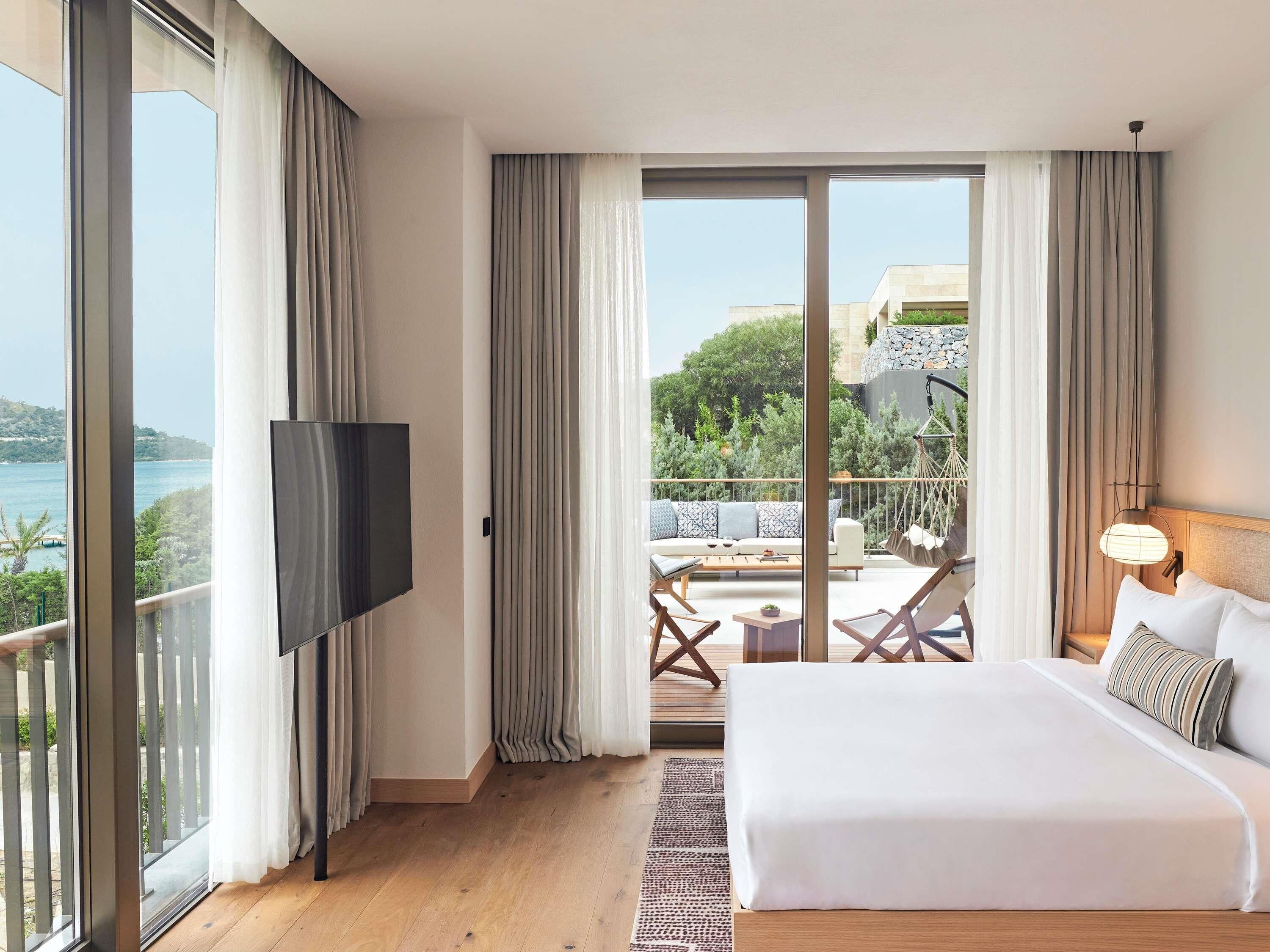 A bedroom with a large bed, a TV, and a balcony with outdoor seating.