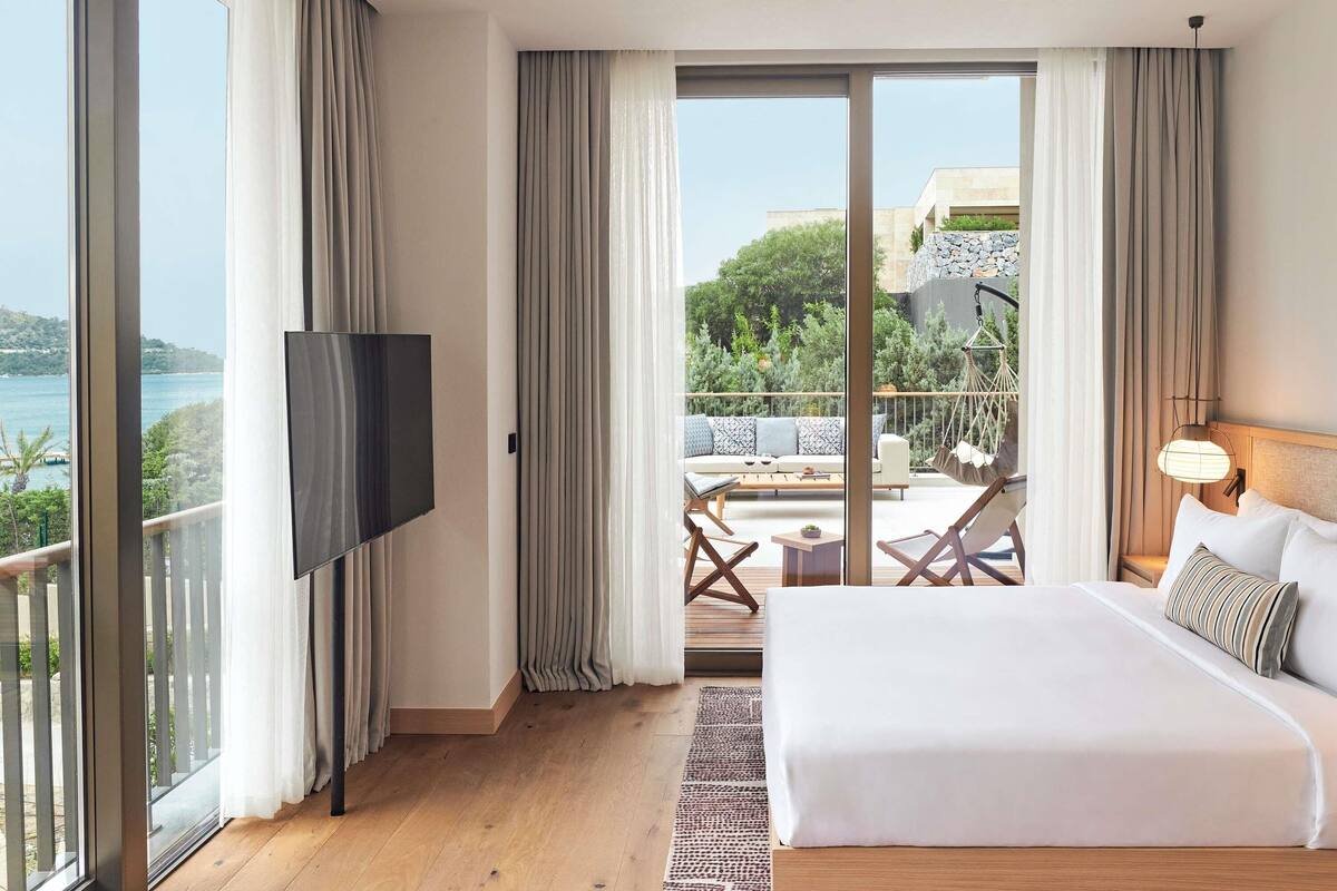 Quarto com uma cama grande, televisão e varanda com área de estar ao ar livre.