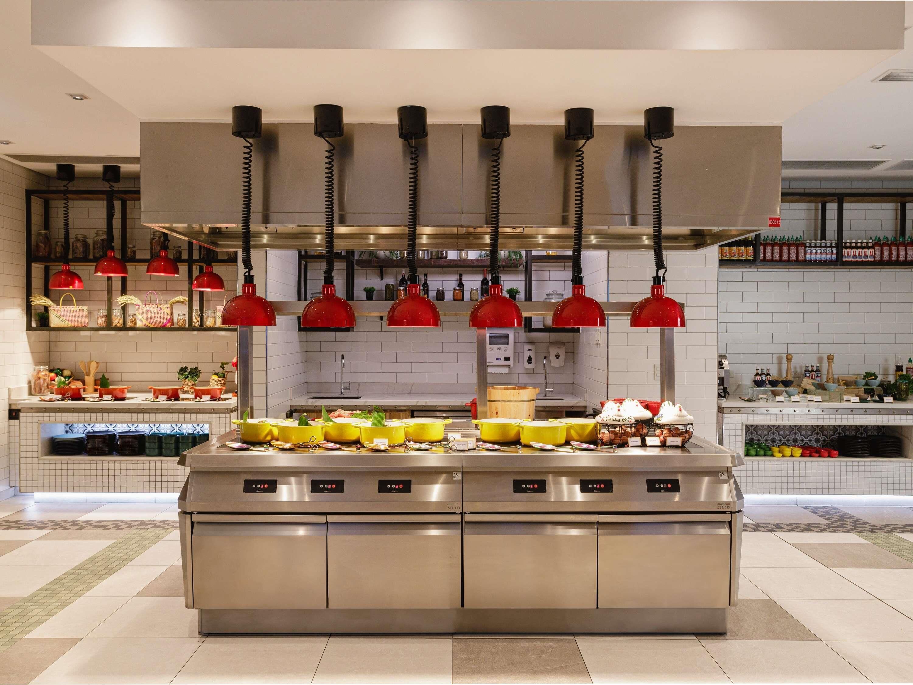 A modern kitchen with stainless steel appliances, red pendant lights, and a variety of food items displayed on the counter.