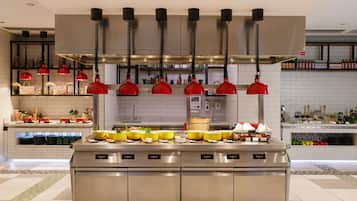A modern kitchen with stainless steel appliances, red pendant lights, and a variety of food items displayed on the counter.