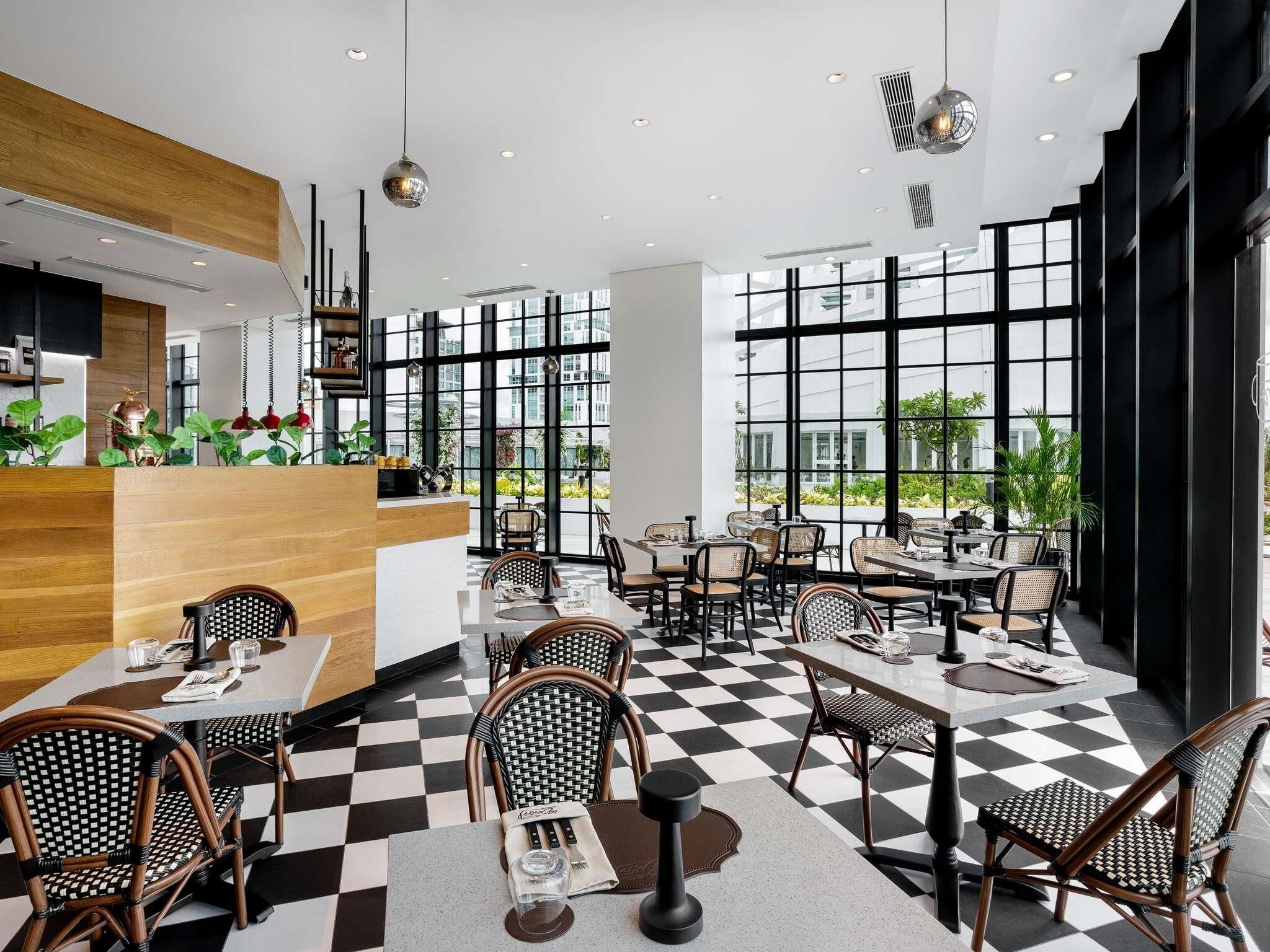 A modern restaurant with checkered flooring, black and white wicker chairs, and large windows offering views of the outdoors.