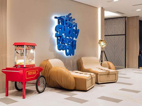 Un interior moderno con una máquina de palomitas rojas, dos sofás color beige y una pared con un letrero de neón azul.