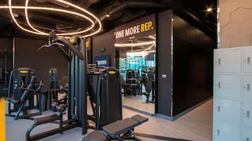 A gym with exercise equipment, a bench, lockers, and a sign that reads 'ONE MORE REP.'