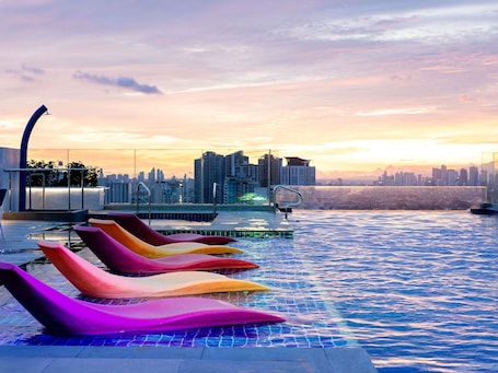 A rooftop infinity pool with colorful lounge chairs, a city skyline in the background, and a sunset.. Ibis Styles Manila Araneta City
