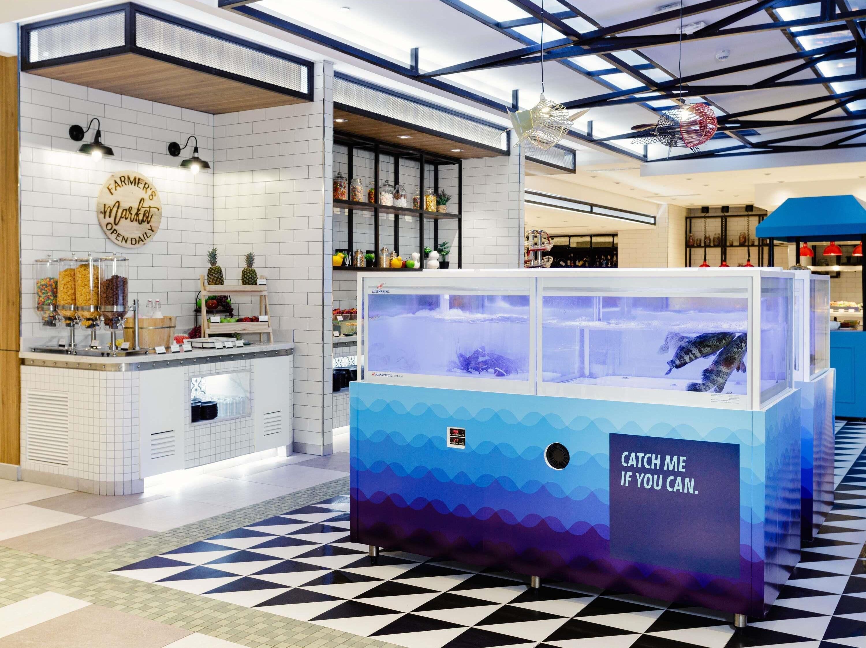 Un espacio interior moderno con piso a cuadros, una barra con frascos de aperitivos y una vitrina azul para peces.