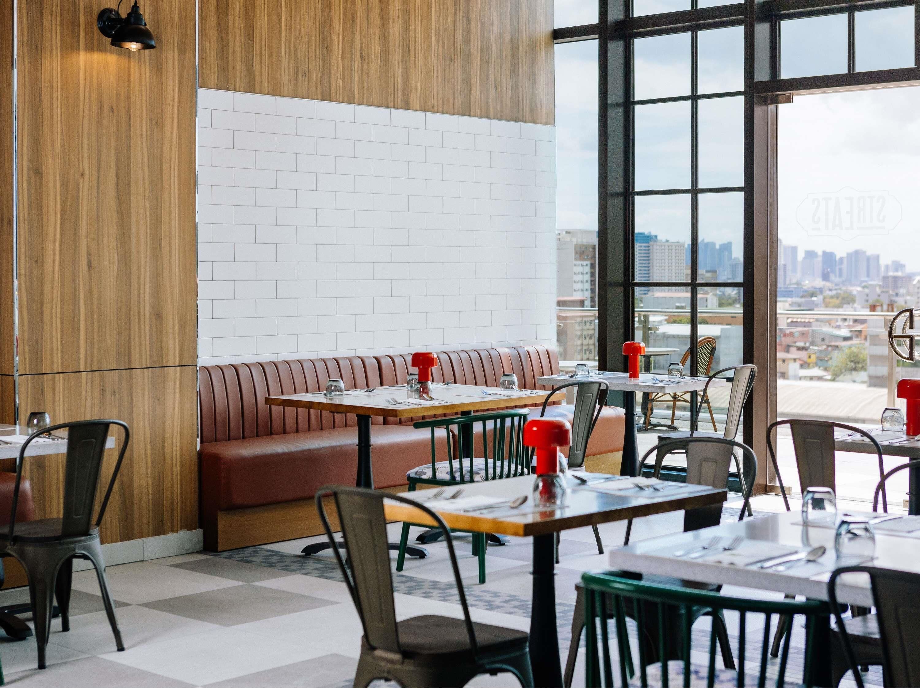 A modern restaurant with a brick wall, wooden panel, and a city view through large windows.