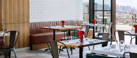 Un restaurant moderne avec un mur en briques, un lambris en bois et une vue sur la ville grâce à de grandes fenêtres.