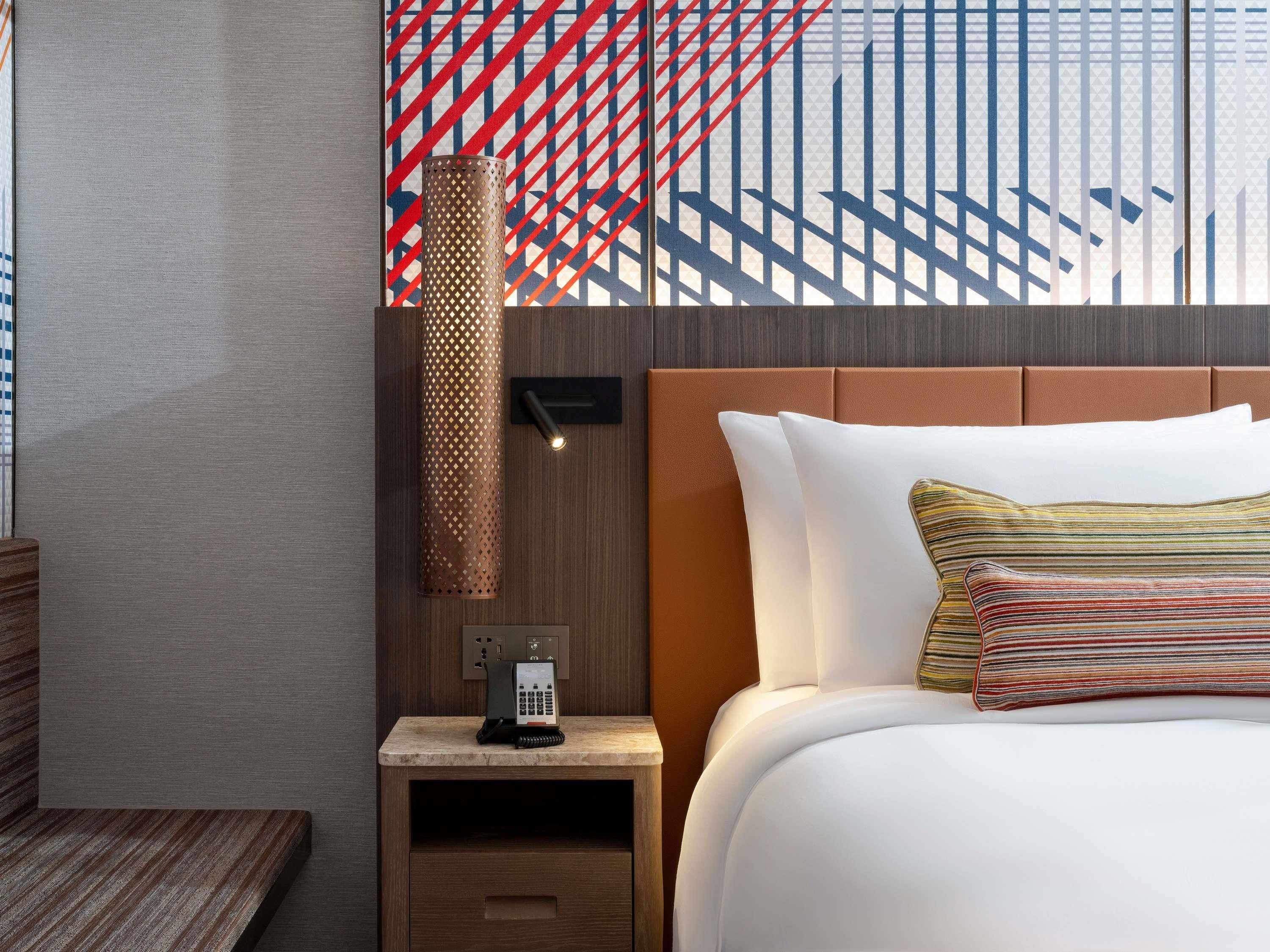 Ein Hotelzimmer mit einem Bett, einem Nachttisch mit Telefon, einer Wandlampe und einer Wand mit Muster.