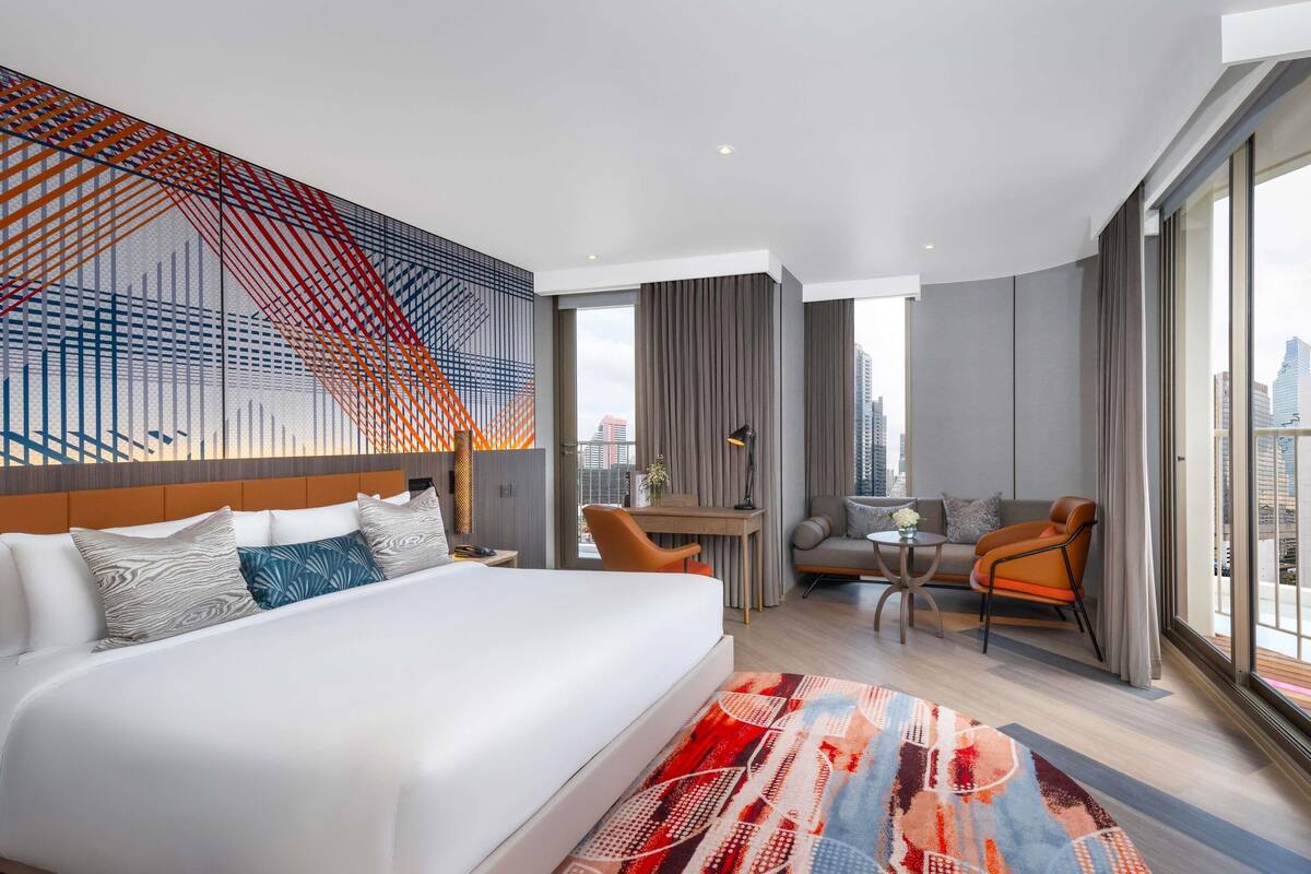 Une chambre d’hôtel moderne, dotée d’un grand lit, d’un bureau, d’un canapé et offrant une vue sur la ville.