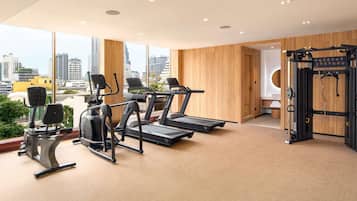 A gym with treadmills, elliptical machines, and weightlifting equipment, large windows with a city view, and wooden panel walls.