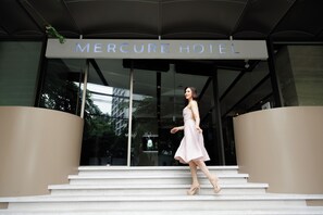 A woman in a light-colored dress and heels walking up the steps to the entrance of the Mercure Hotel. - Mercure Bangkok Surawong (Bangkok)