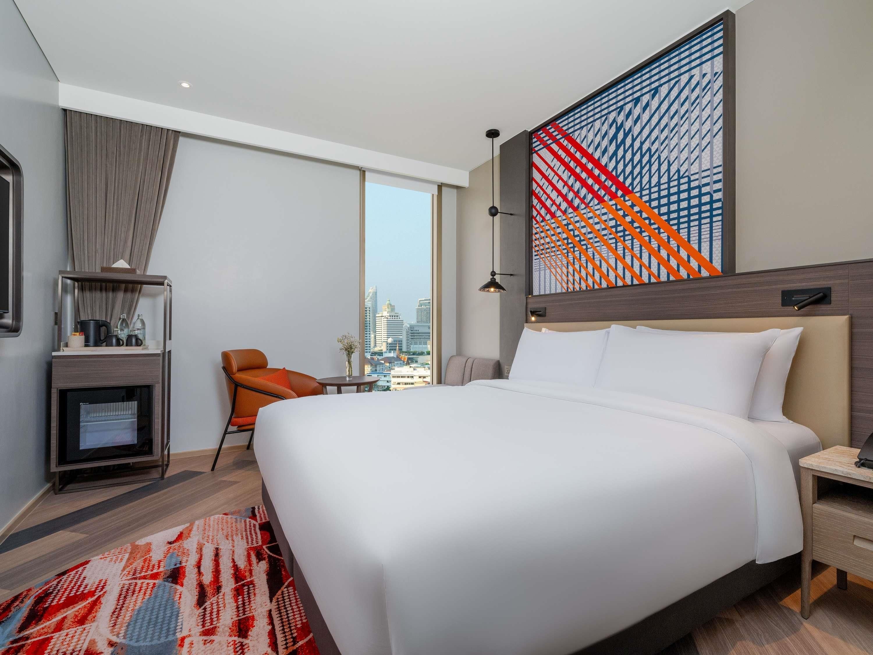 Een moderne hotelkamer met een groot bed, een bureau, een stoel, een televisie en uitzicht over de stad.