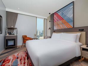 Una habitación de hotel moderna con una cama grande, un escritorio, una silla, un televisor y vistas a la ciudad.