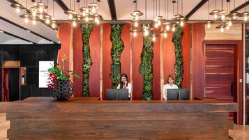 A reception desk with a wooden finish, two receptionists, and a wall with vertical wooden slats and greenery.