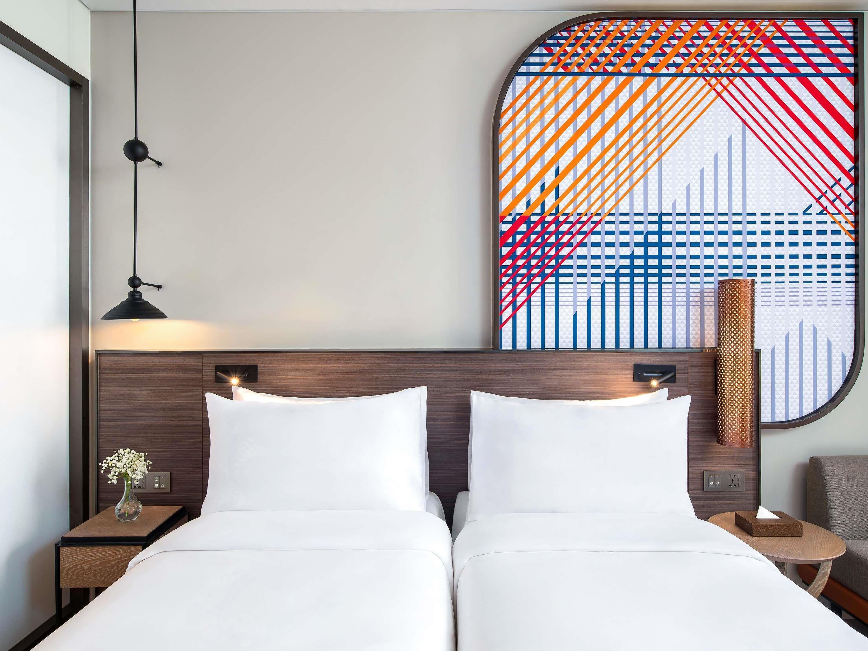 Habitación de hotel con una cama doble, una mesita de noche con un florero, una lámpara de pared y un adorno en la pared.