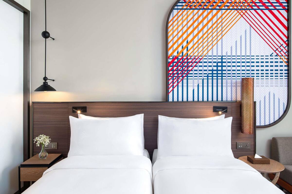 Une chambre d’hôtel avec un lit double, une table de chevet avec un vase, une lampe fixée au mur et un élément décoratif mural.
