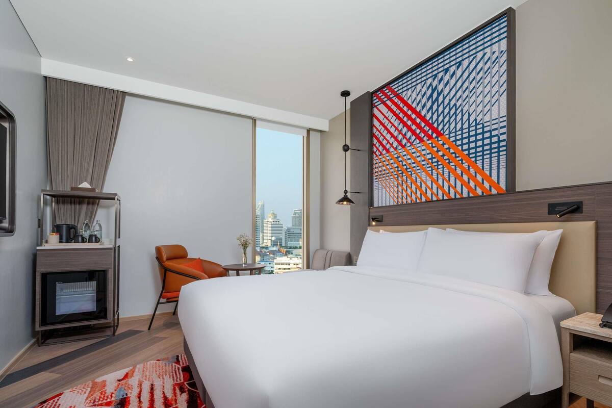 Une chambre d’hôtel moderne dotée d’un grand lit, d’un bureau, d’une chaise, d’une télévision et offrant une vue sur la ville.
