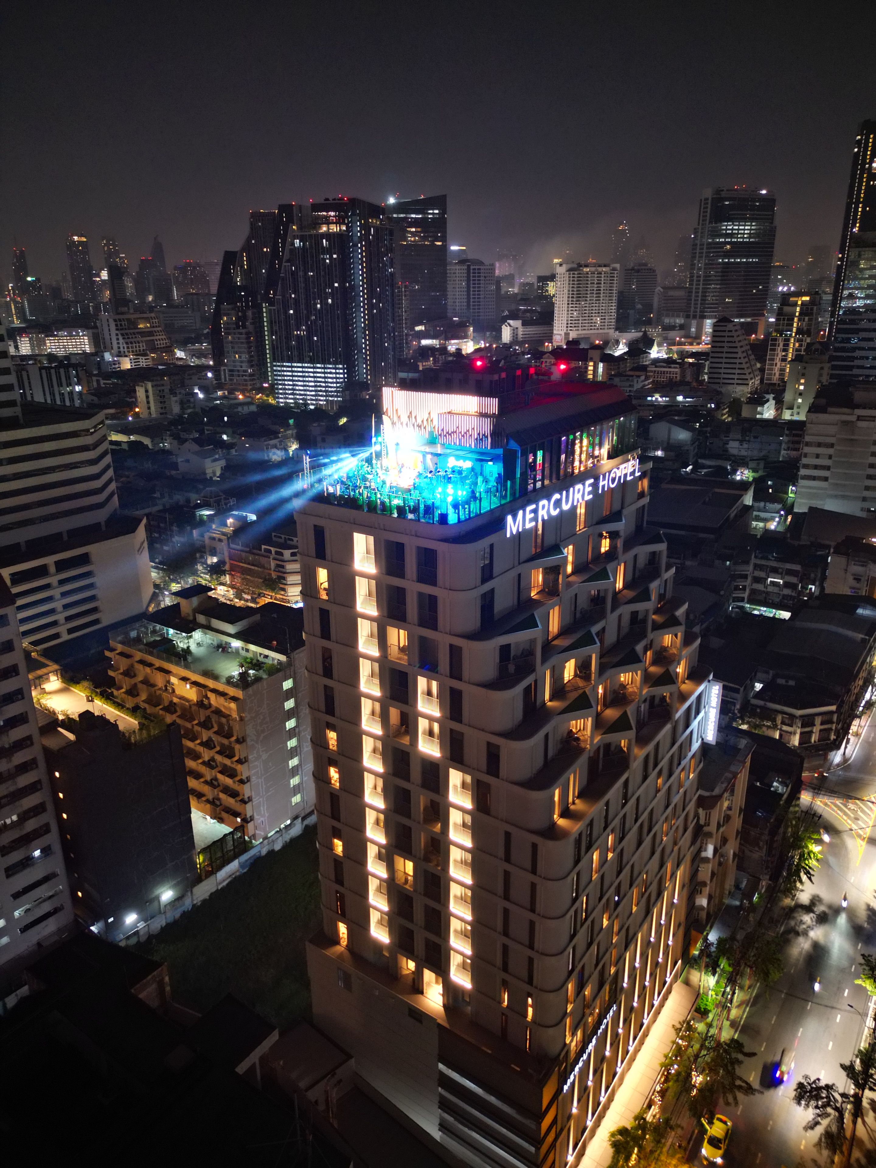 Ein Hochhotel mit mehreren Etagen, einer Dachterrasse und einer gut beleuchteten Fassade.