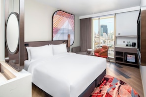 Habitación de hotel con una cama grande, un escritorio, un televisor de pantalla plana, una silla y vistas a la ciudad.