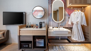 Een moderne hotelkamer met een flatscreen televisie, een koffiezetapparaat, een magnetron, een wastafel met spiegel, en een badjas hangend bij de deur.