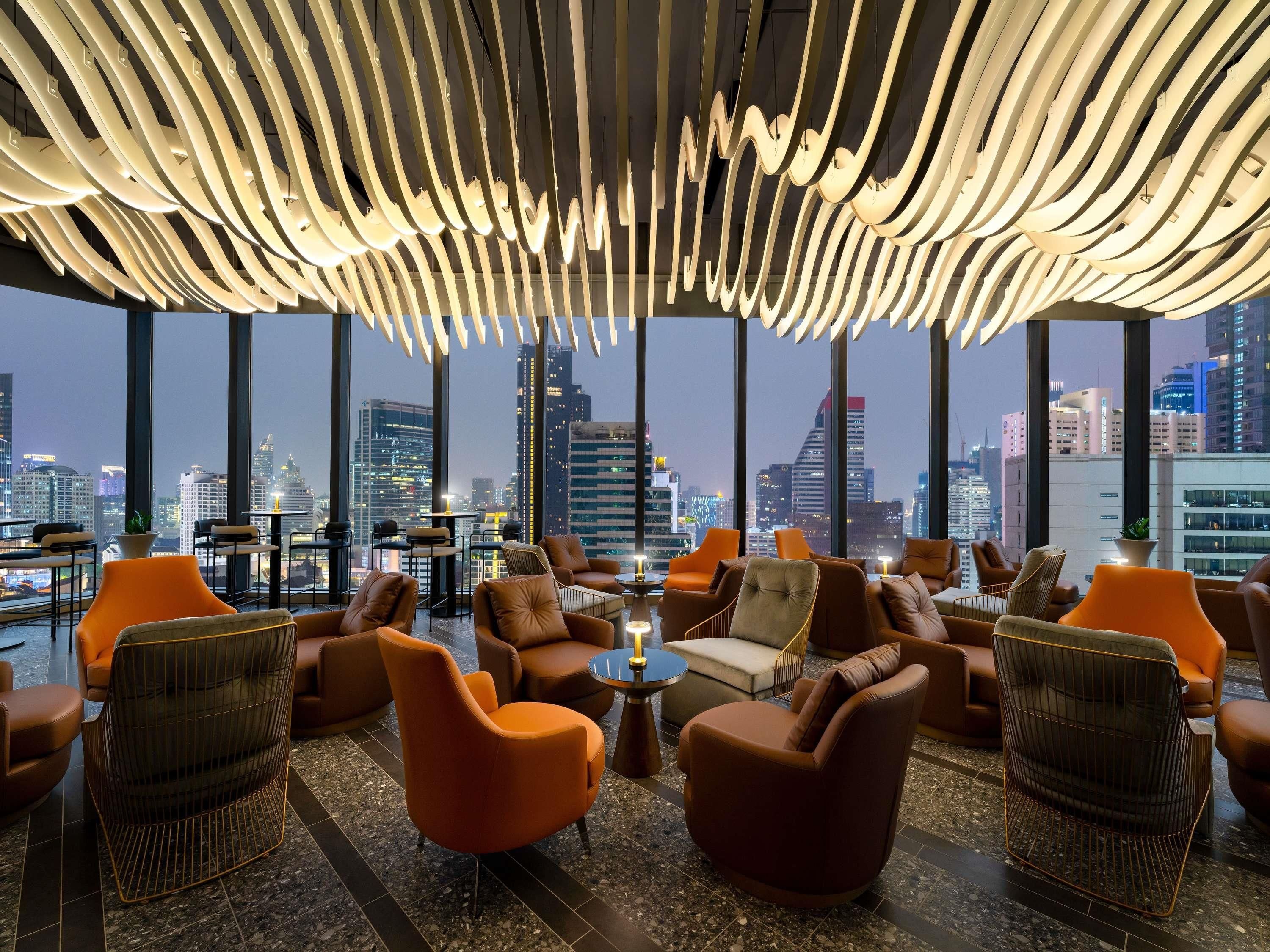 A modern lounge with leather chairs, a high ceiling with unique lighting, and a city view.