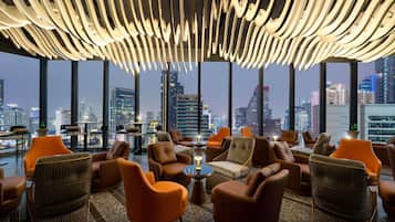 Un salón moderno con sillones de cuero, techo alto con iluminación original y vistas a la ciudad.