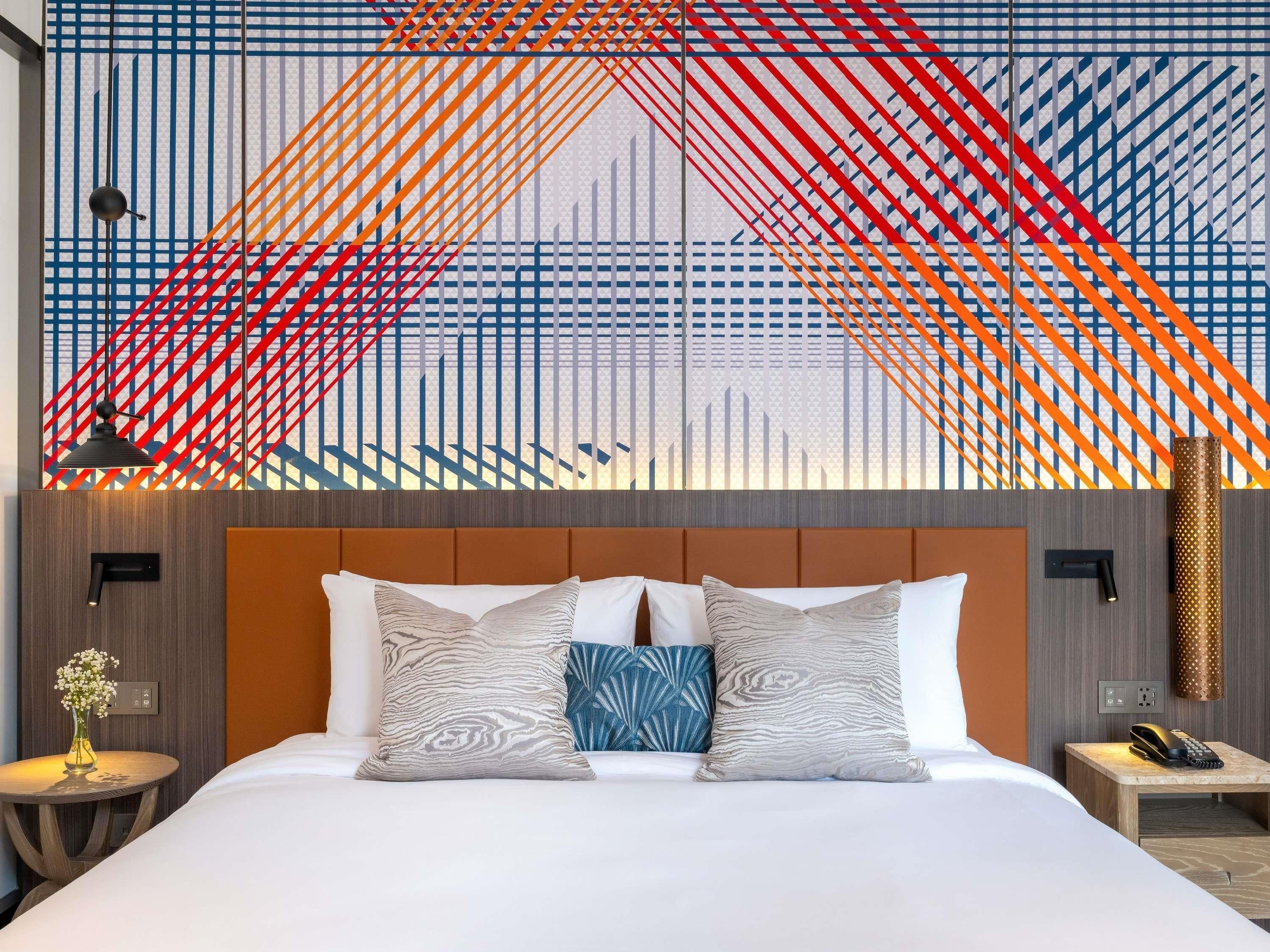 A hotel room with a large bed, two bedside tables, a wall-mounted telephone, and a decorative wall panel.
