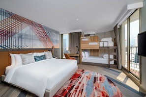 A modern hotel room with a large bed, a bunk bed, a desk, and a TV.