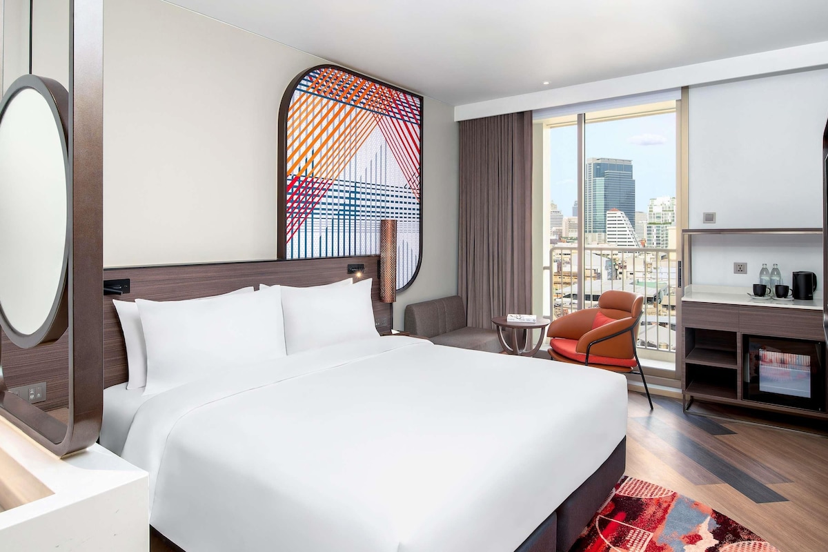 Une chambre d’hôtel moderne, dotée d’un grand lit, d’un bureau, d’une chaise et offrant une vue sur la ville.