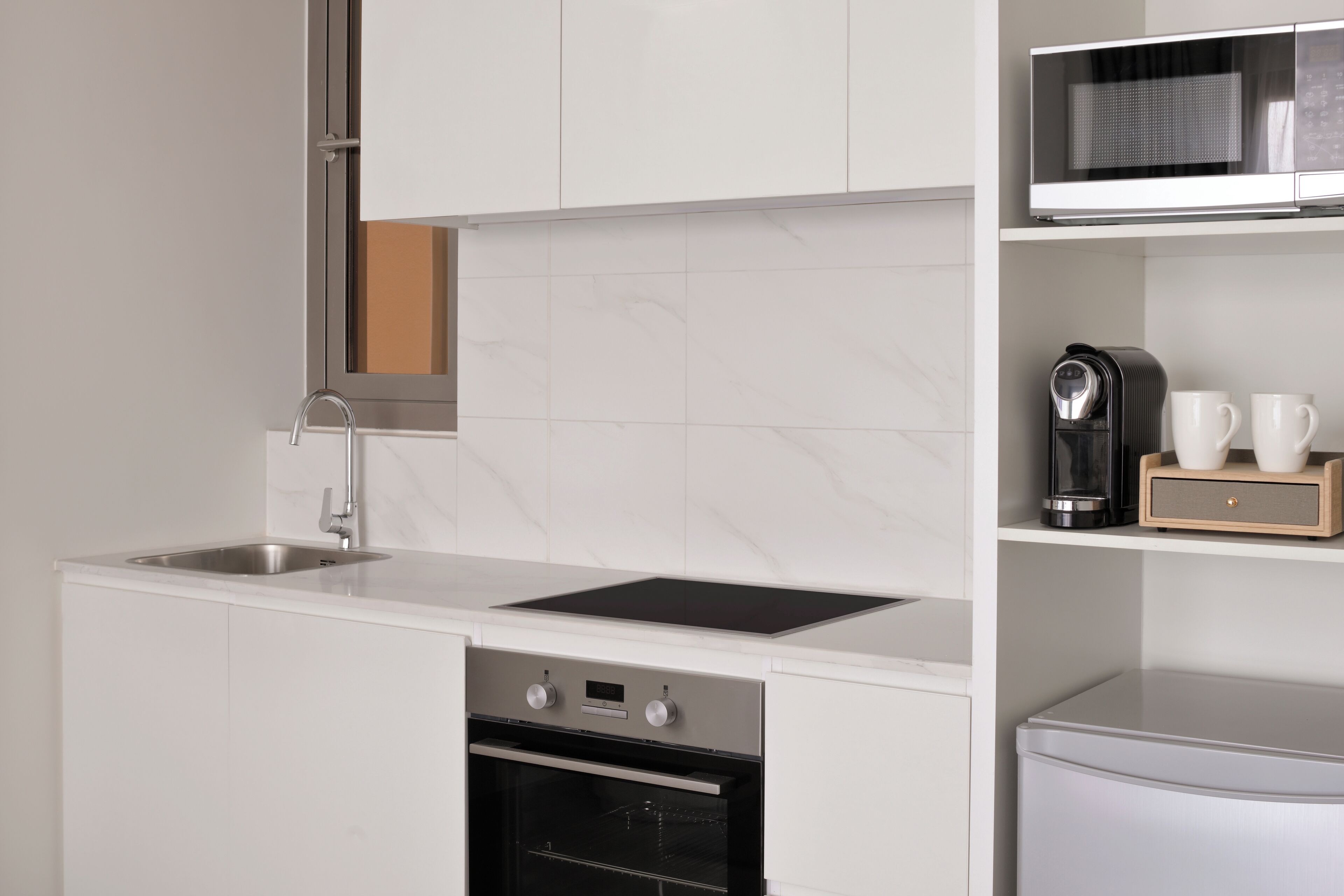A modern kitchen with white cabinetry, a stainless steel sink, a built-in oven, and a microwave on a shelf.