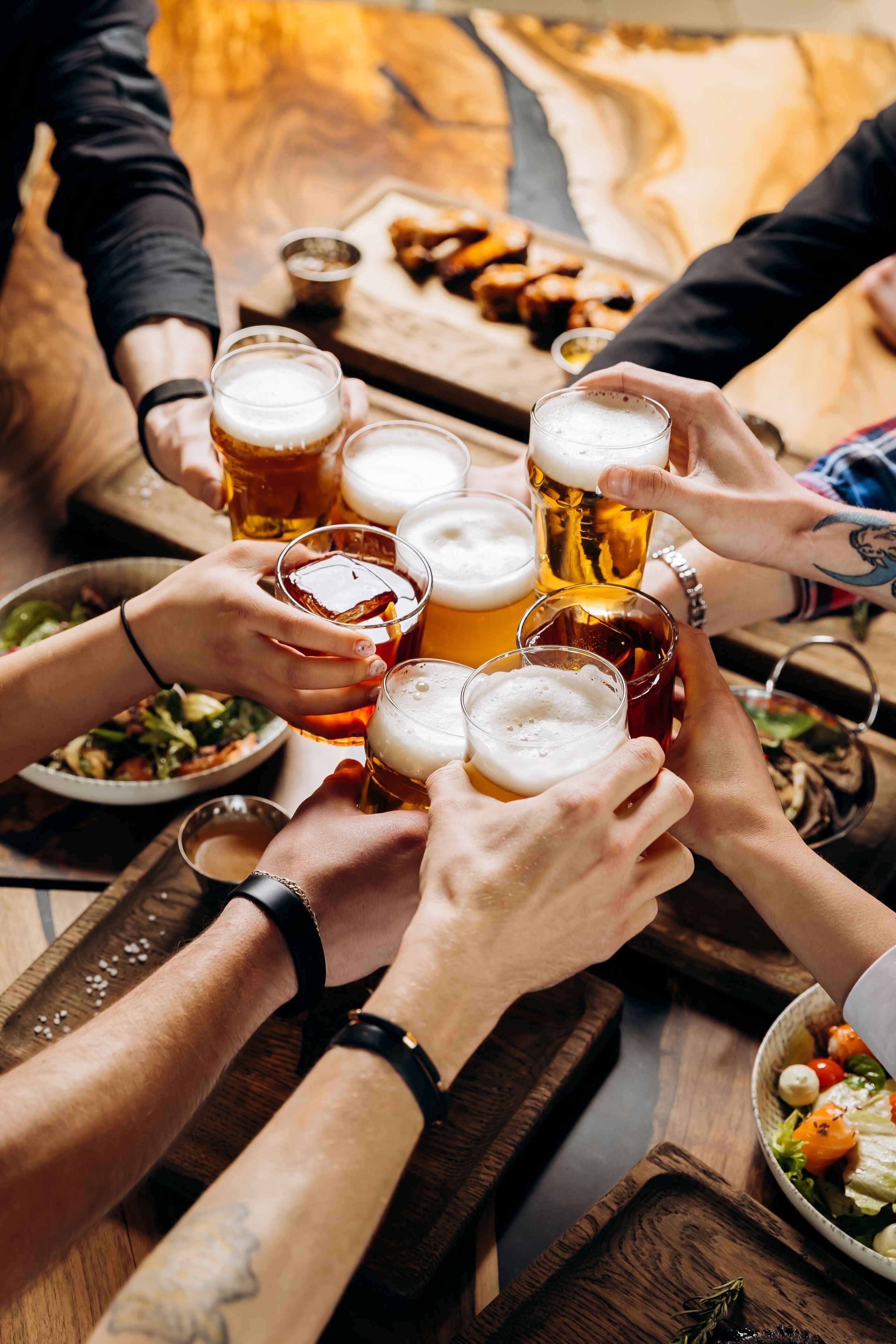 Un grupo de personas brindando con jarras de cerveza alrededor de una mesa de madera con comida.