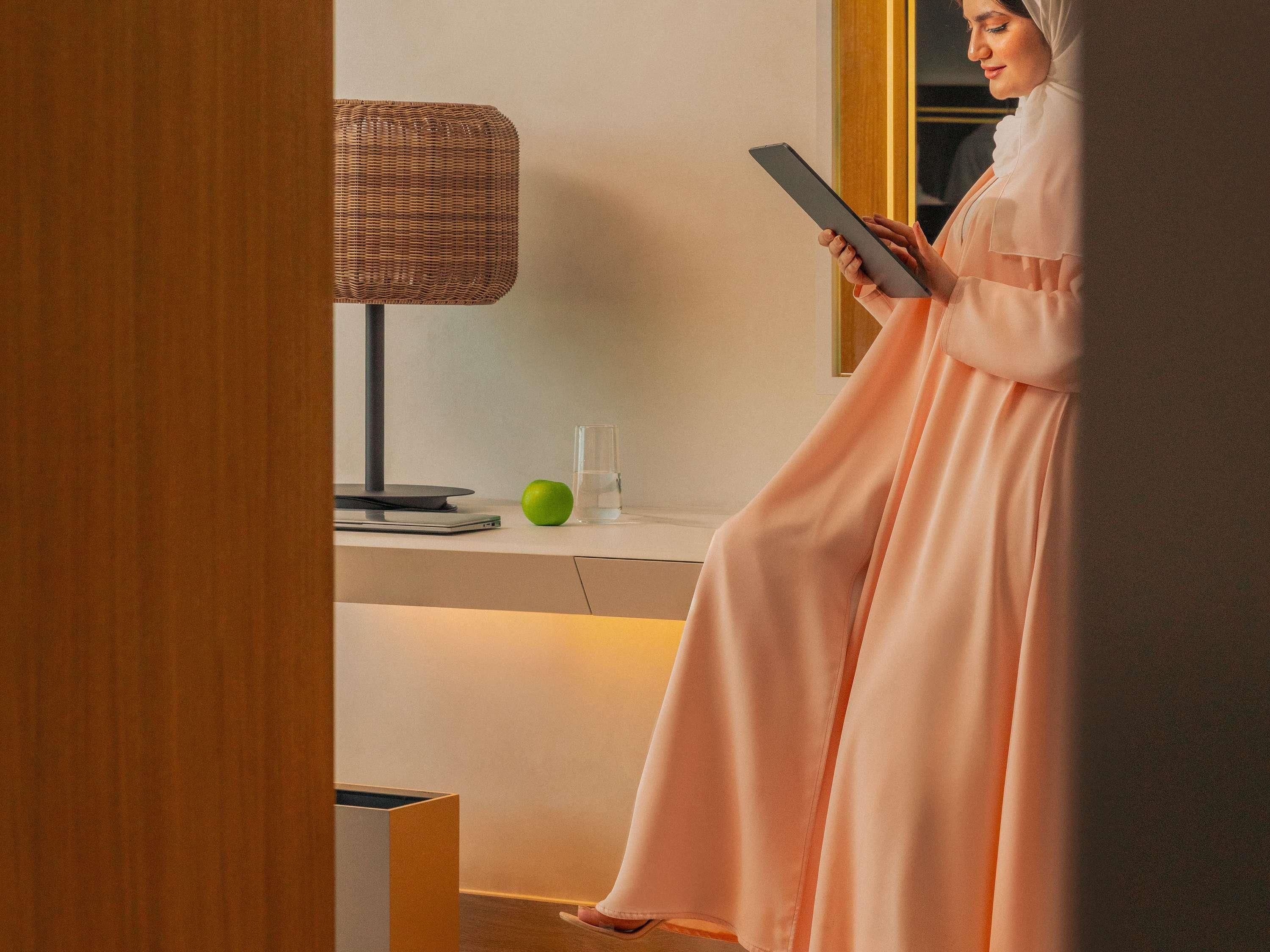 Ein Zimmer mit einer modernen Lampe, einem Glas Wasser, einem grünen Apfel und einer Person, die ein Tablet hält.