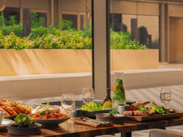 A dining table with various dishes and drinks, set against a backdrop of a building and greenery.