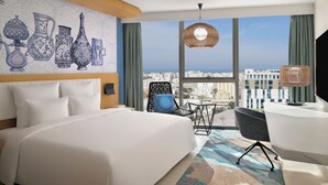 A modern hotel room with a large bed, a desk, and a view of the city.