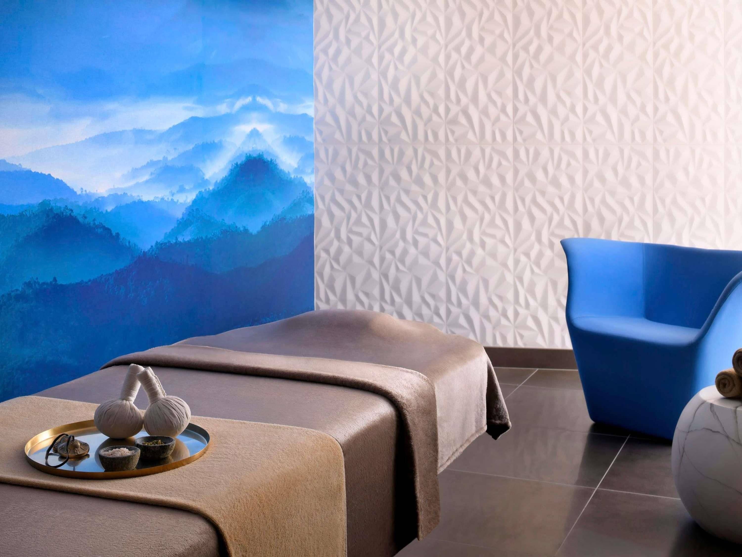 Una mesa de masaje con una bandeja de utensilios y una silla azul en un spa con vistas a la montaña.