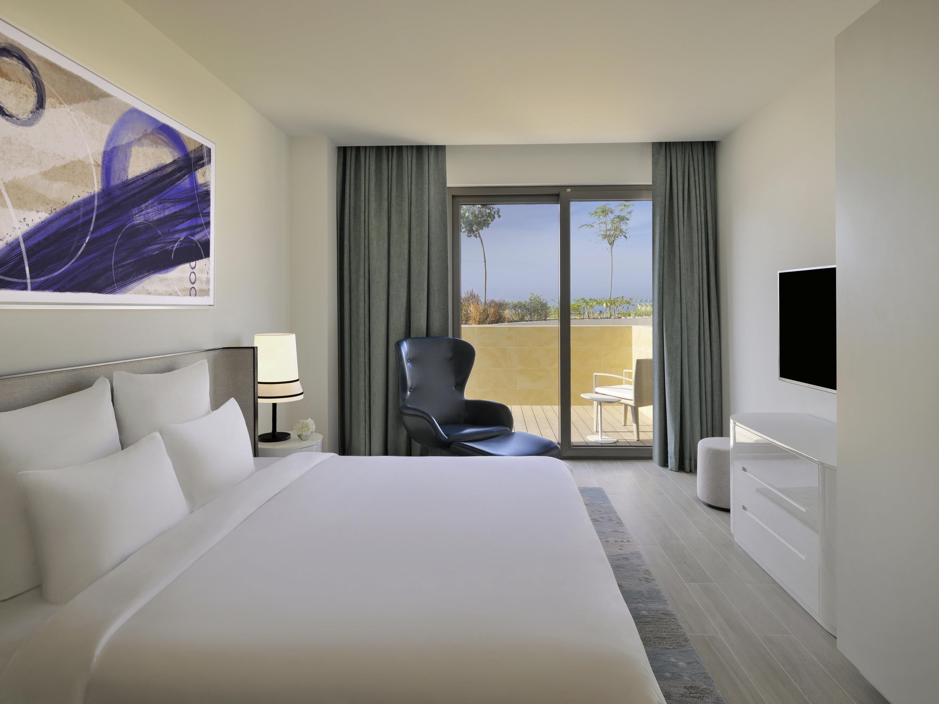 Une chambre d’hôtel avec un grand lit, une chaise, une télévision et un balcon avec vue.