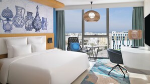 A modern hotel room with a large bed, a desk, and a view of the city.