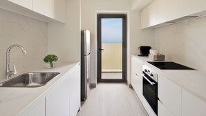 A modern kitchen with white cabinetry, a stainless steel sink, a black stove, and a view through a door to a balcony.