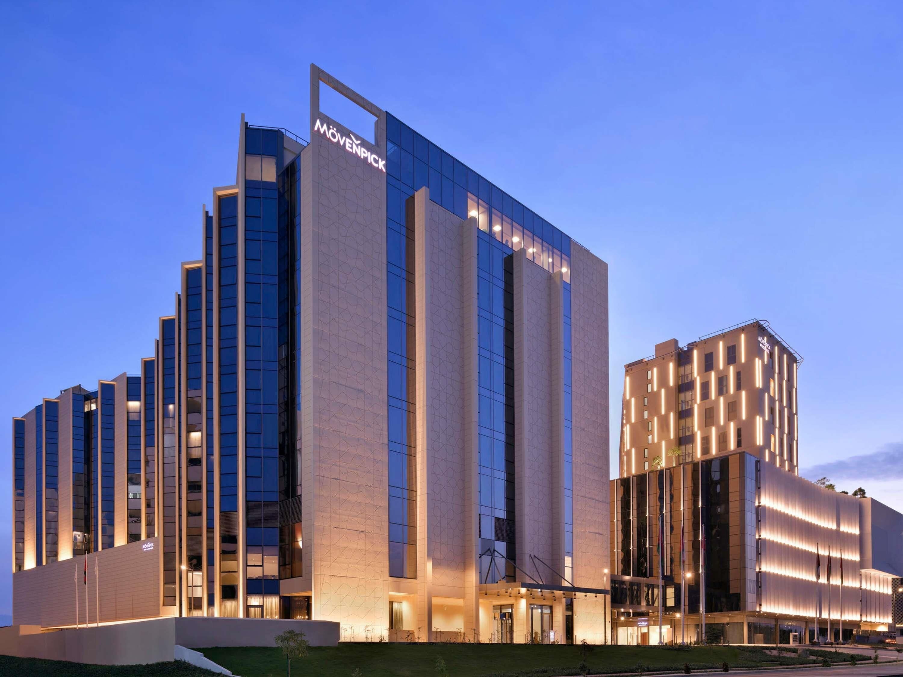 Un hotel moderno con un llamativo letrero de 'Mövenpick', con fachada de vidrio y un diseño geométrico en el exterior.