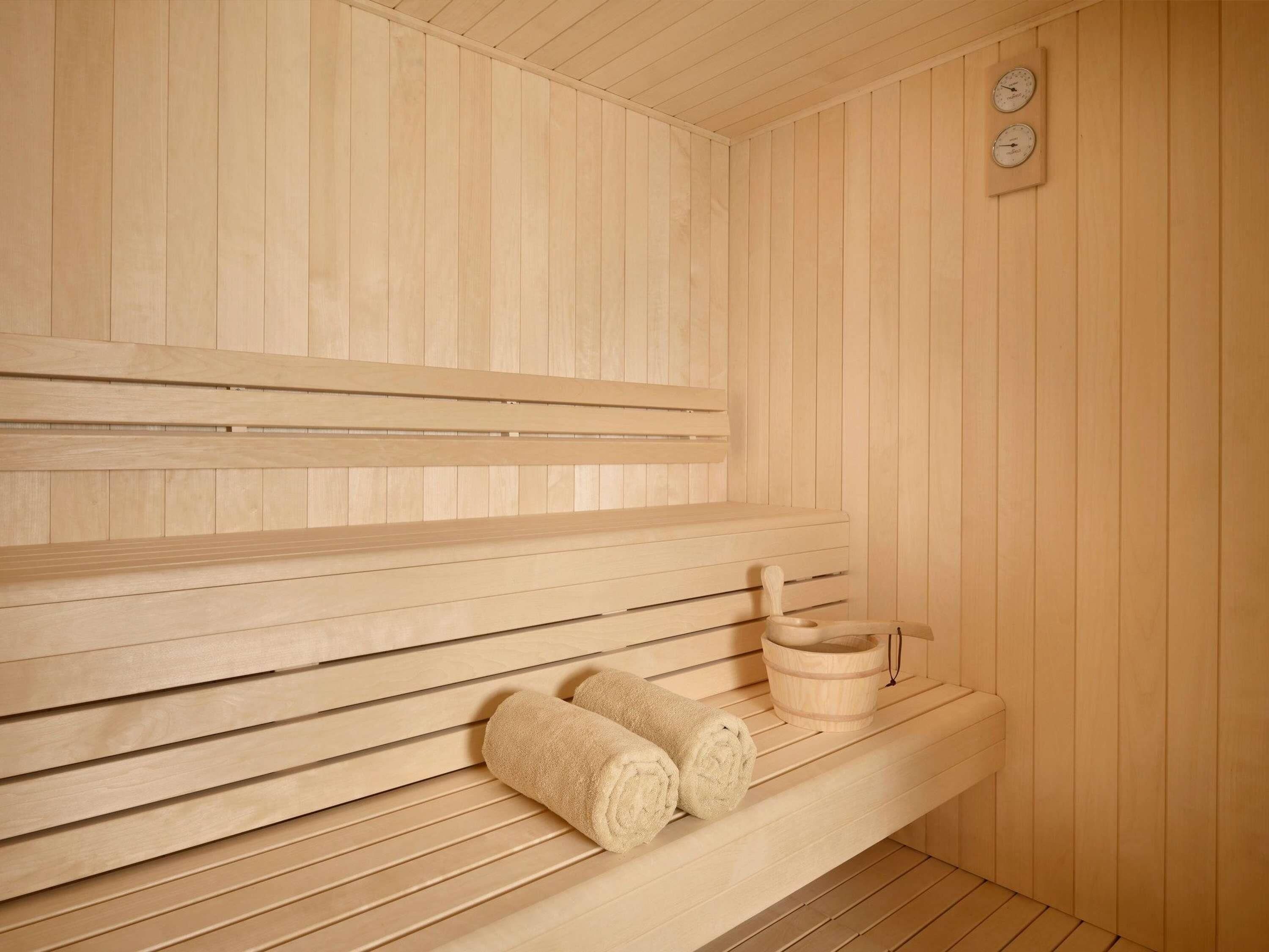 Un sauna avec des bancs en bois, un banc avec des serviettes et un seau en bois.