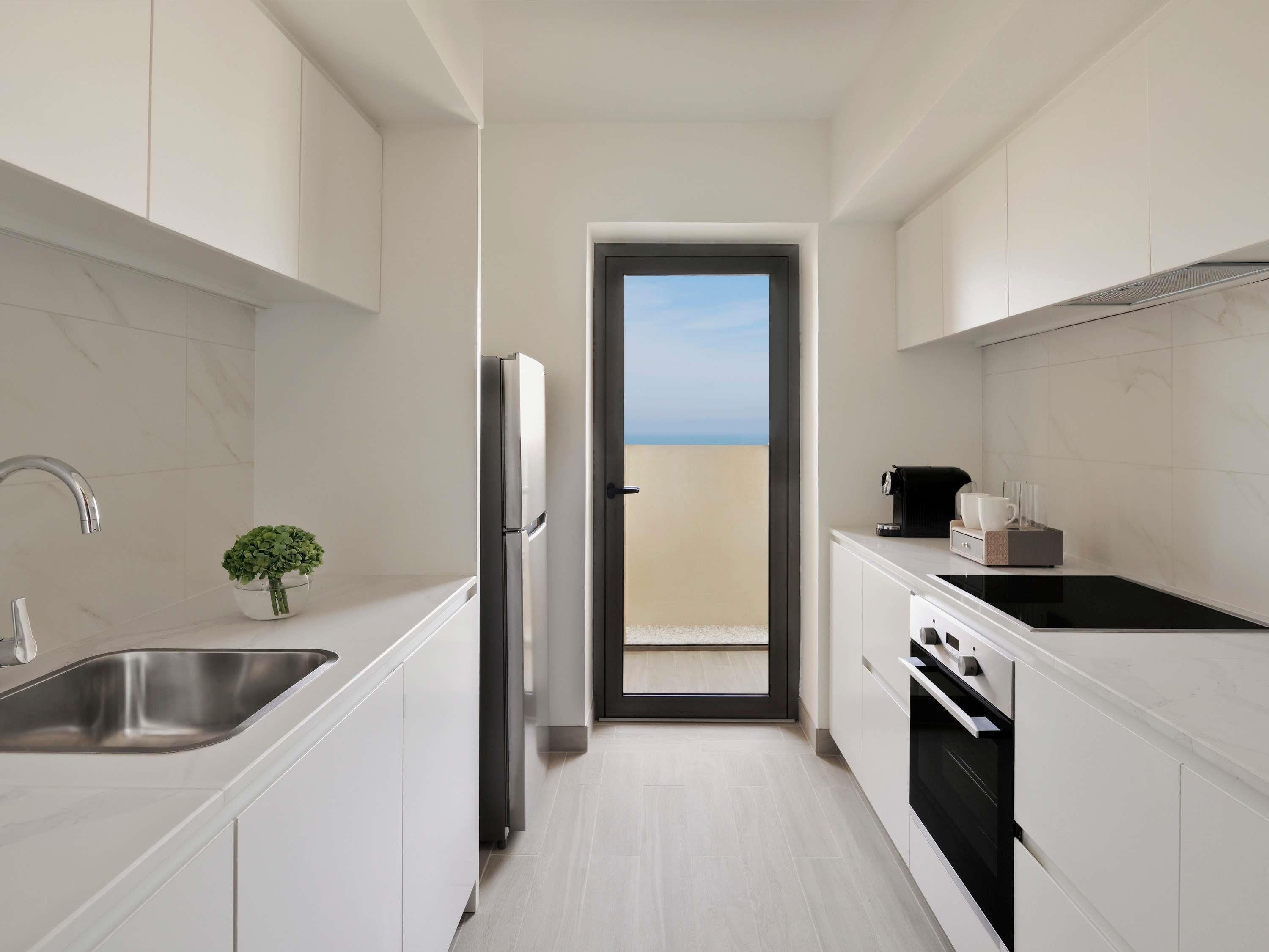 A modern kitchen with white cabinetry, a stainless steel sink, a refrigerator, and an oven. There is a small potted plant on the counter.