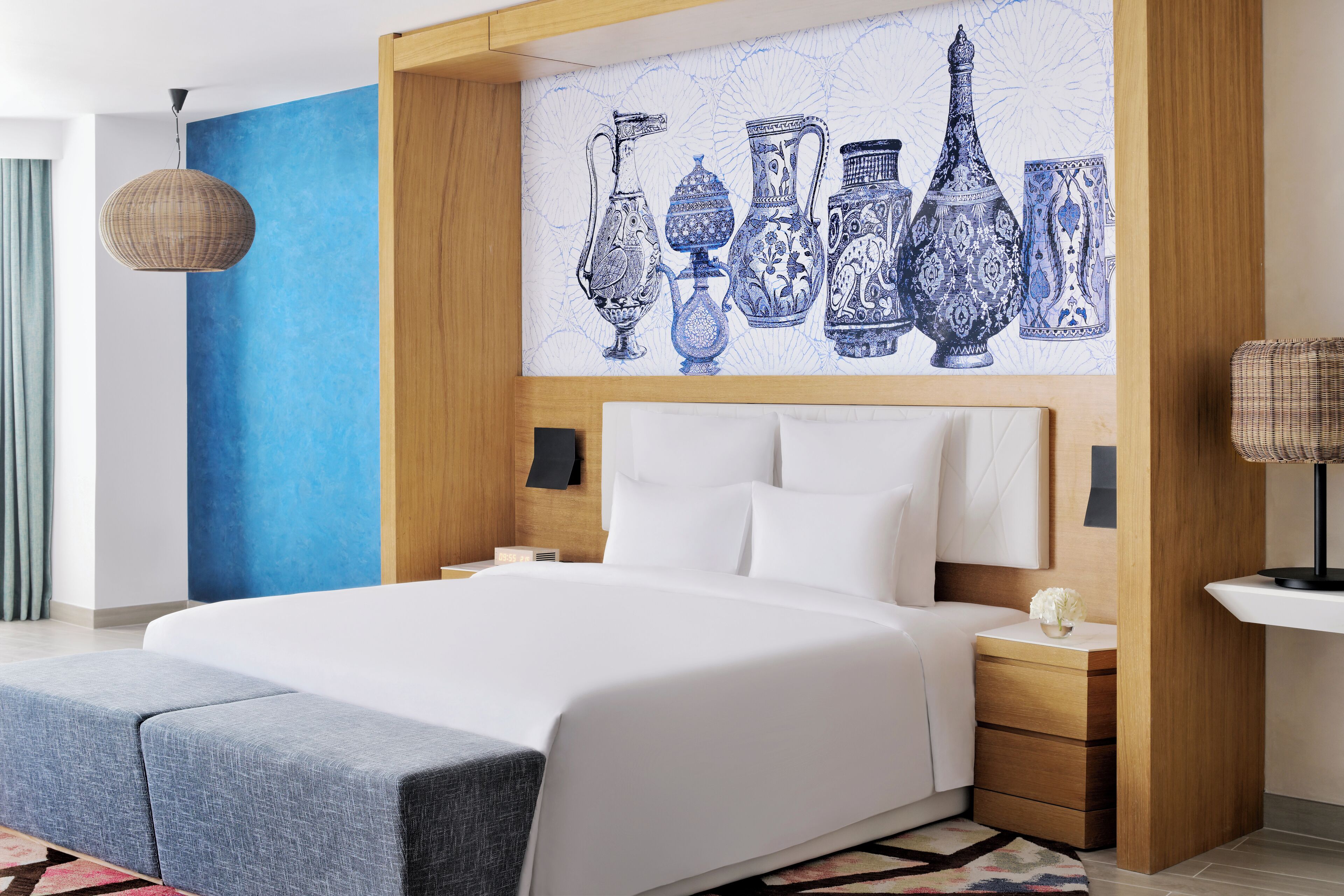 A modern hotel room with a large bed, a blue accent wall, and a wall art of vases.