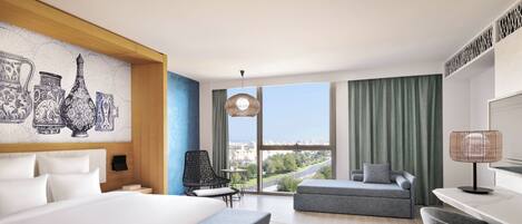A modern hotel room with a large bed, a desk, a chair, a sofa, and a view of the city through large windows.