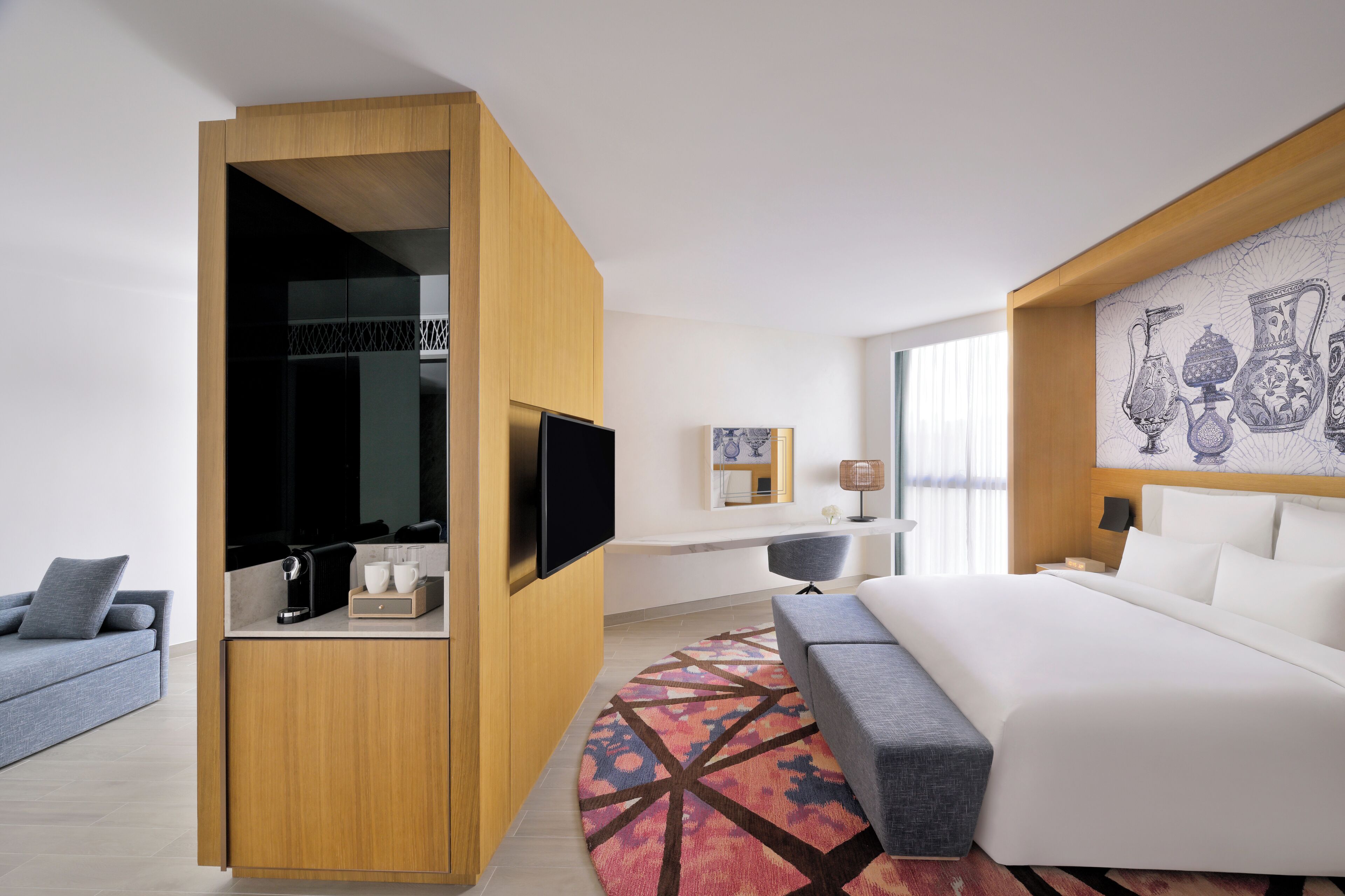 Habitación de hotel moderna con una cama grande, un armario de madera, un televisor de pantalla plana, un escritorio y una pared decorada con jarrones.