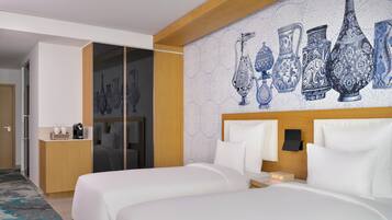 Een hotelkamer met twee bedden, een nachtkastje, een wandklok en een decoratieve muur met blauwe patronen.