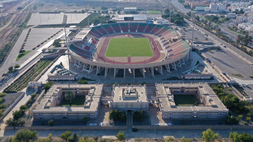 Vista aérea de un estadio con campo central, áreas de asientos y estacionamiento.