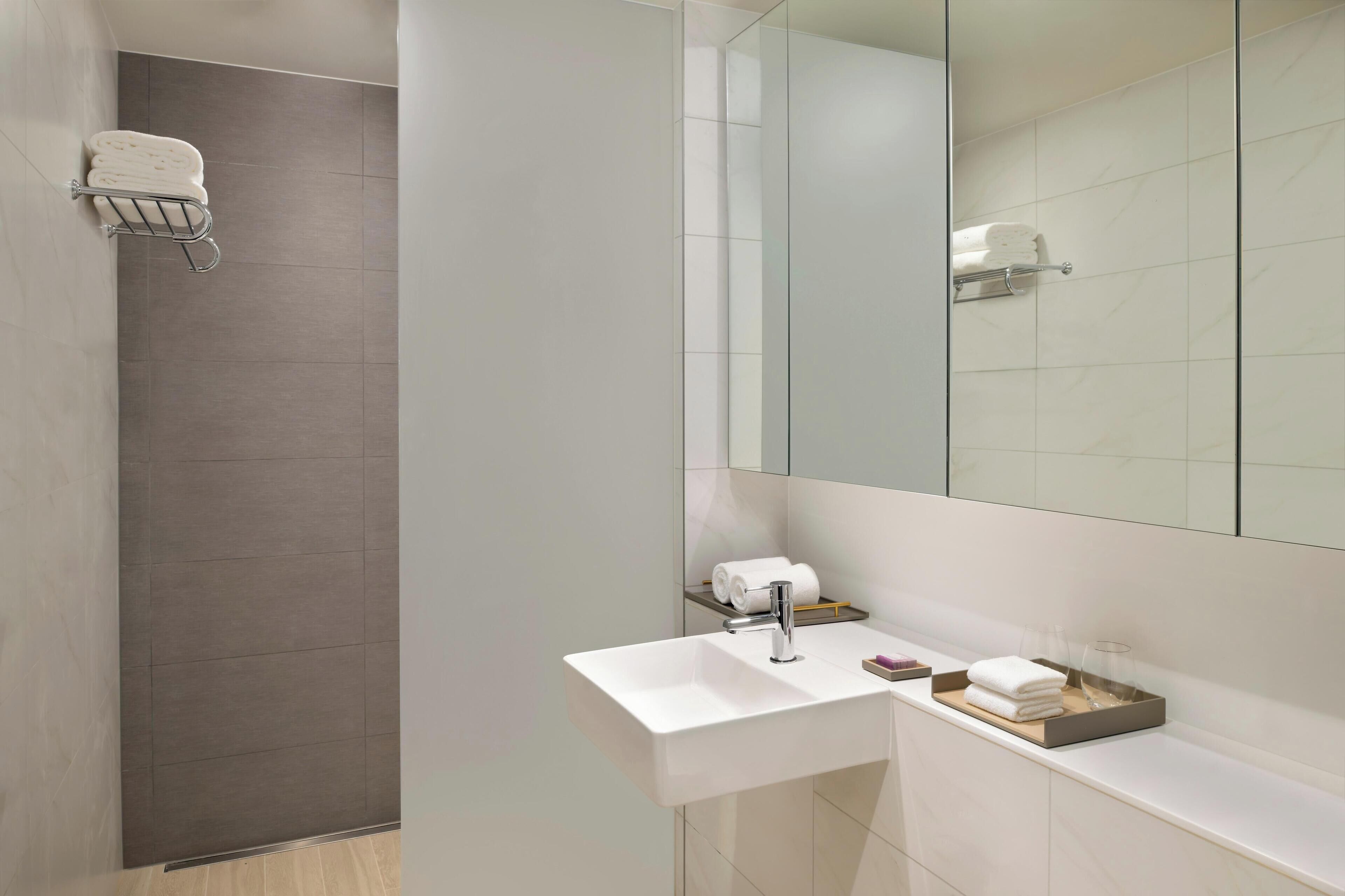 A modern bathroom with a white sink, a mirror, and a shower area.
