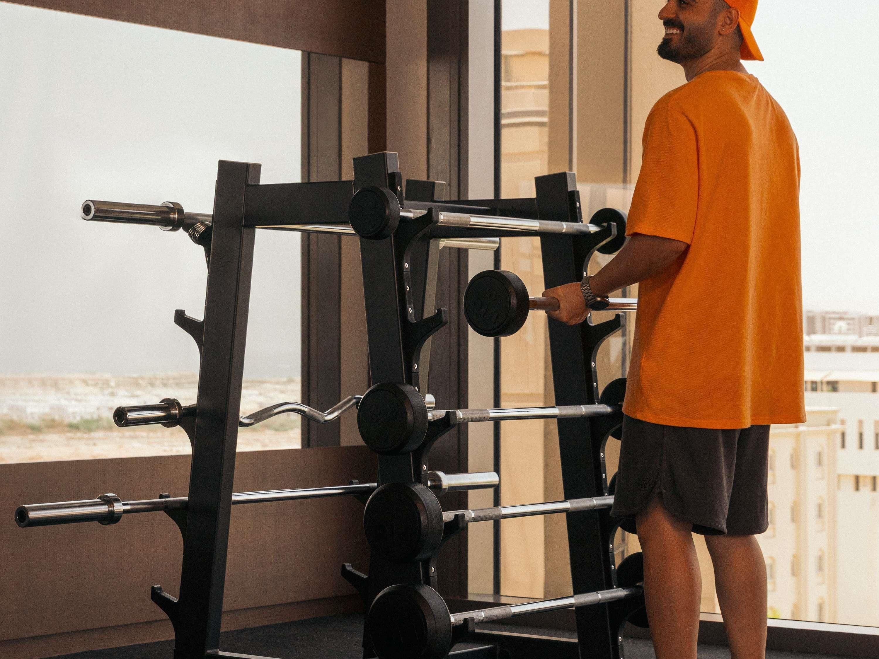 A person exercising with a weight bench and dumbbells in a gym with large windows.
