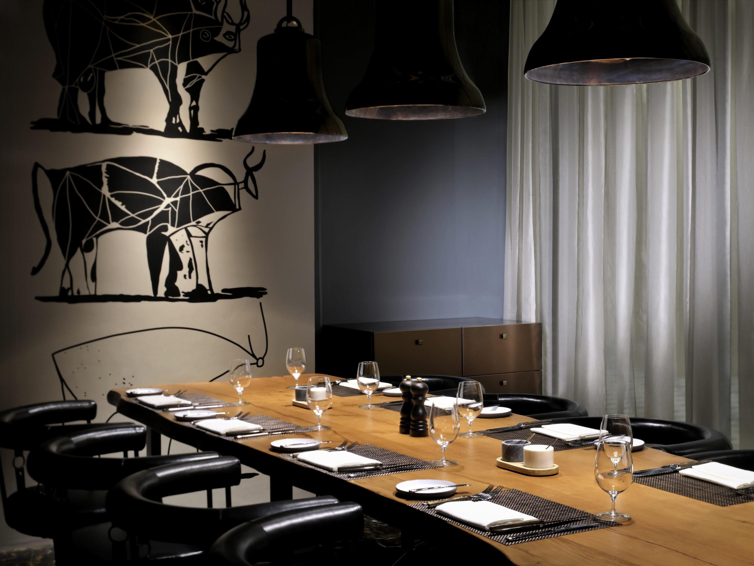 Un comedor con una mesa larga lista para una comida, sillas negras e iluminación colgante.